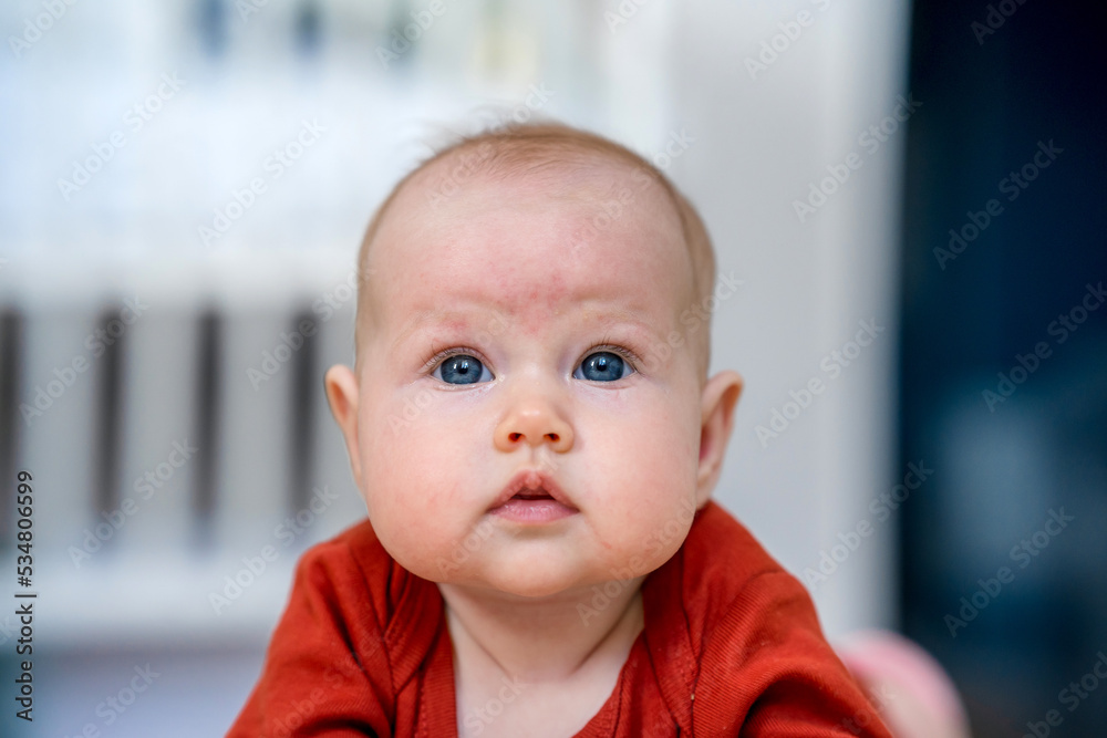 Close-up portrait of a cute Caucasian newborn baby. Charming funny baby looking into the camera. An authentic childhood and a candid lifestyle moment.