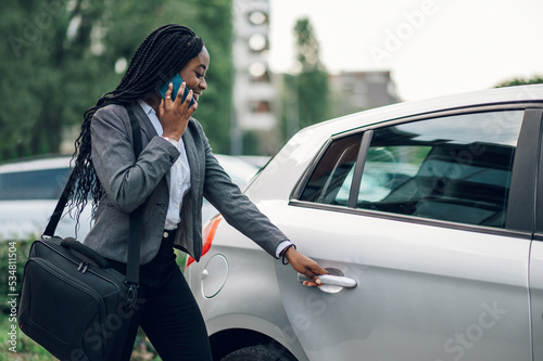 African american business woman getting into the car and using smartphone © Zamrznuti tonovi