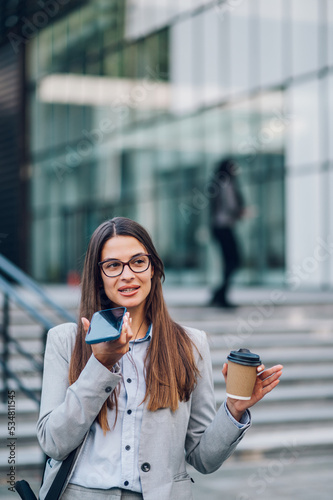Business woman standing outside while using a smartphone and drinking coffee