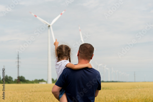 A girl and her dad look at the wind generator in the field. Ecology. Future.