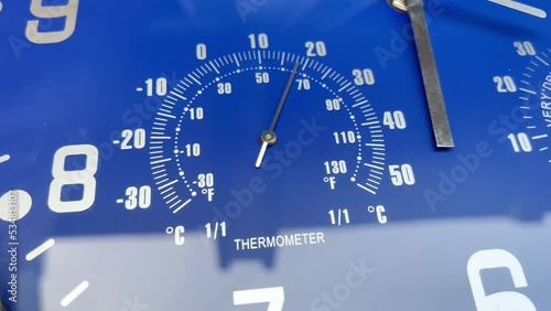 A thermometer with a mechanical arrow measuring air temperature on a blue background. Thermometer measuring the air temperature on the dial of a large clock on a blue background. Old classic thermomet photo