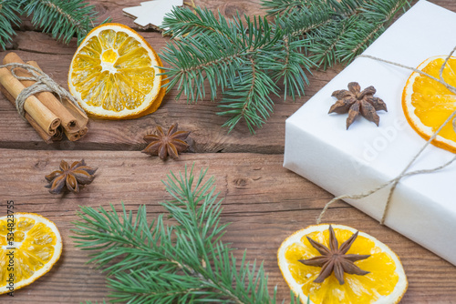 Christmas presents or gift box wrapped in kraft paper with decorations, pine cones, dry orange orange slices, cinnamon and fir branches on a rustic wooden background. Holiday concept.