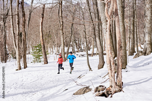 Athletic couple in bright jackets running in winter forest.