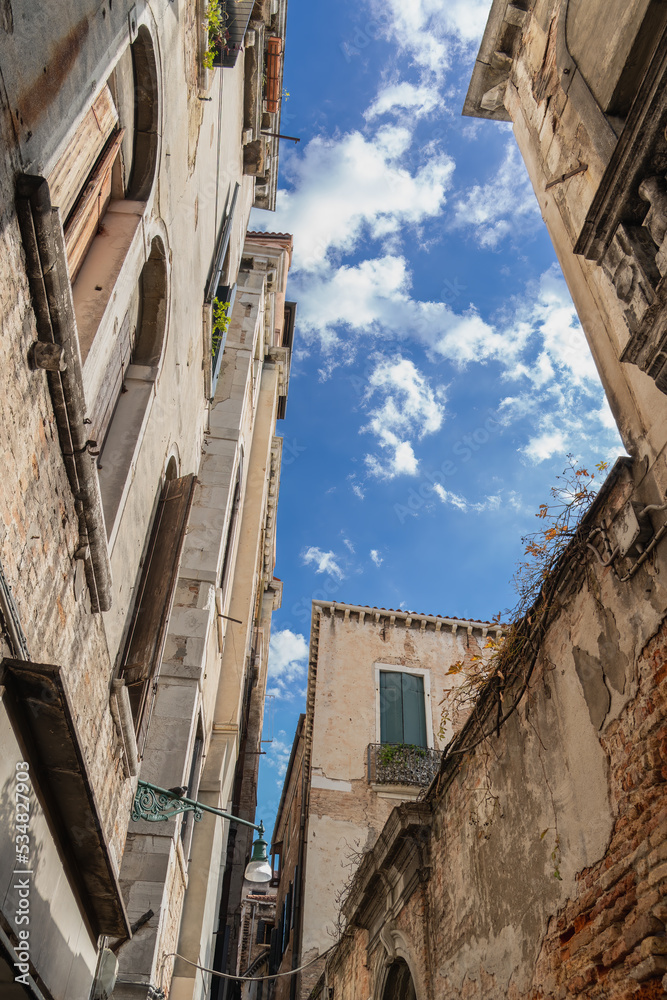 Vintage walls with high windows under blue sky with white clouds in Venice on a sunny morning, wooden shutters on Venetian windows, old buildings, texture of old walls in Venice, view from below