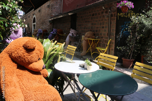 Photography Big lonely colorful teddy bears are sitting sadly around the table in a street c