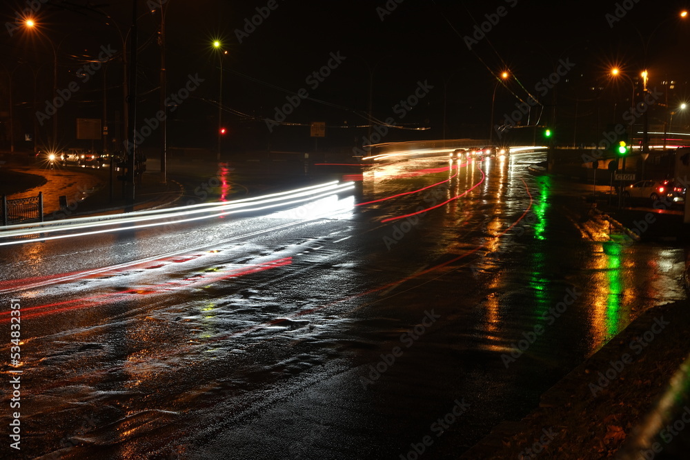 Lights of cars at night. Street lights. Night city. Long-exposure photograph night road. Colored bands of light on the road. Wet road after rain.