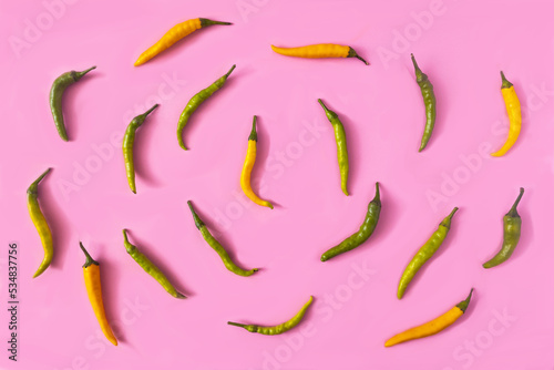Green and yellow spicy peppers aligned in circles on pink background. Minimal creative concept for wallpaper or food advertisement. Flat lay. Copy space