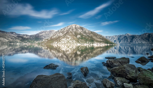 Panoromic reflection of mountains on sea with blue sky and clouds on top © Aytug Bayer