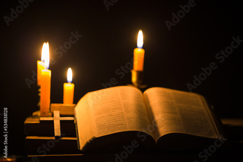 Light candle with holy bible and cross or crucifix on old wooden background in church.Candlelight and open book on vintage wood table christianity study and reading in home.Concept of christ religion