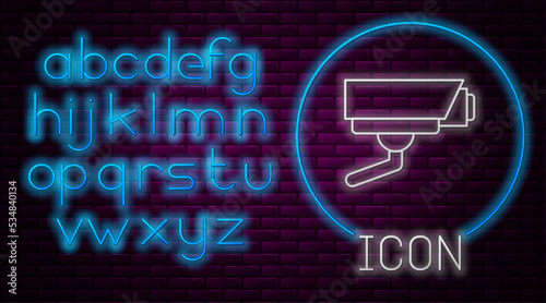Glowing neon line Security camera icon isolated on brick wall background. Neon light alphabet. Vector