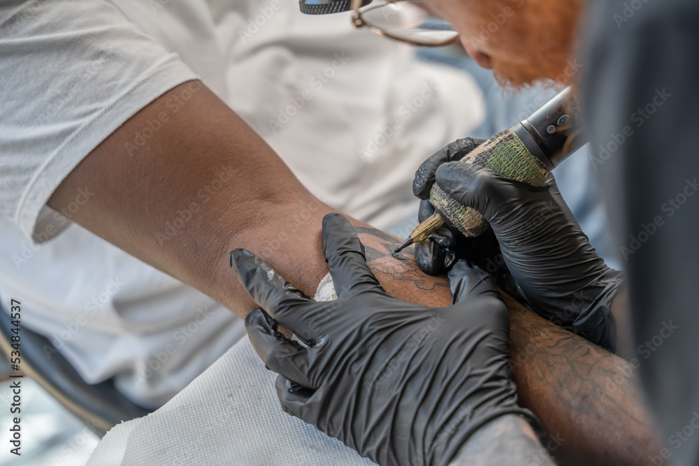 Mains d'un tatoueur en train de tatouer sur la peau d'un avant bras