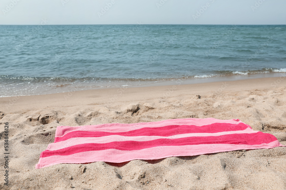 Pink striped towel on beach sand near sea Pink striped towel on beach sand near sea