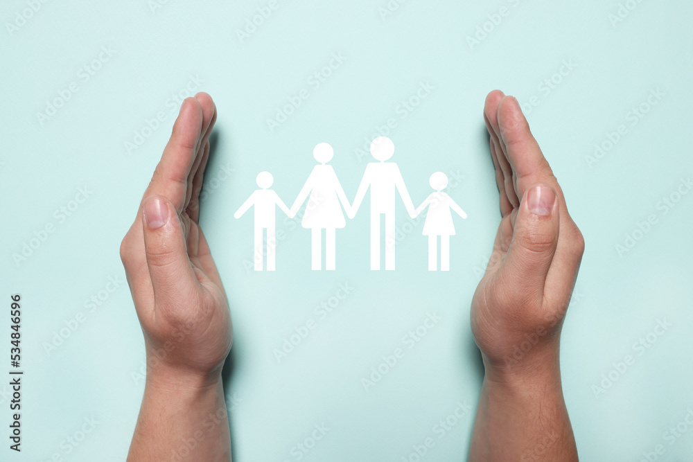 Man holding hands around cutout paper silhouette of family on light blue background, top view. Insurance concept Man holding hands around cutout paper silhouette of family on light blue background, top view. Insurance concept