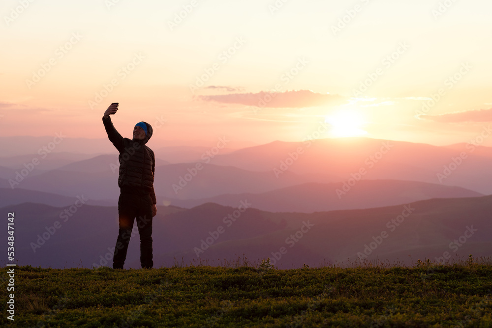 Man takes a selfie on the phone against the background of sunset in the mountains