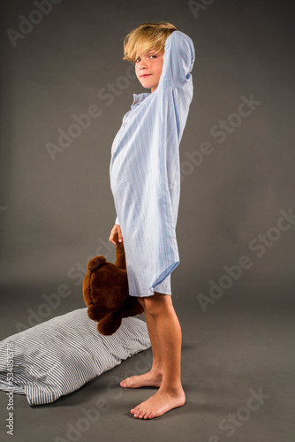Cute little boy standing in his nightshirt while holding his stuffed bear