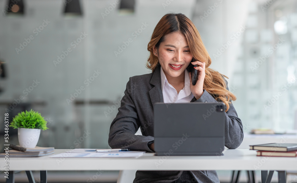 Smiling Asian Businesswoman writing notes while making phone call and using tablet laptop at workplease, Smiling Asian Businesswoman writing notes while making phone call and using tablet laptop at workplease,
