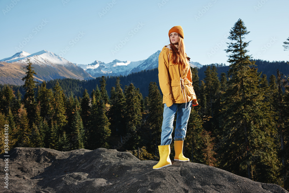Woman in full height smile with teeth happiness and laughter tourist in yellow raincoat stands on a mountain trip in the fall and hiking in the mountains in the sunset sunshine freedom