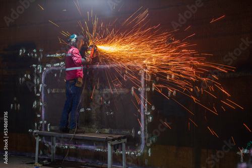 Worker using electric wheel spark grinding on welder metal carbon steel part shell plate inside tank