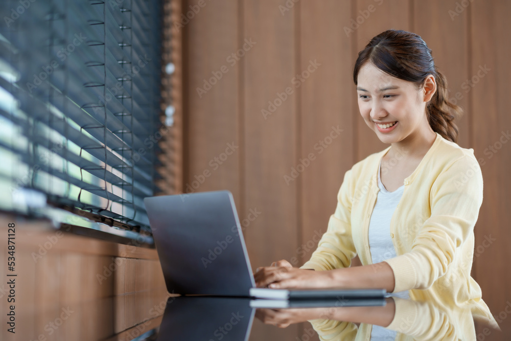 Cute young Asian woman sitting at cafe with her laptop happily. Asia female working on laptop computer at home. Cute young Asian woman sitting at cafe with her laptop happily. Asia female working on laptop computer at home.