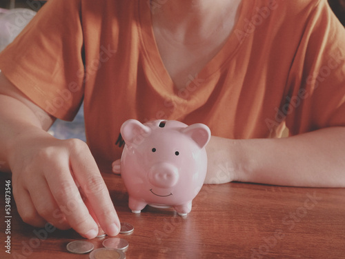 woman hand putting money coin into piggy for saving money wealth and financial concept on wood table