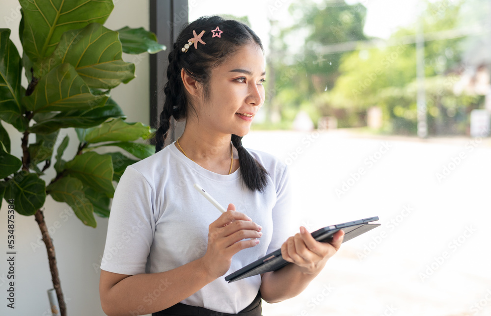 Image of young asian woman, company worker in glasses, smiling and holding digital tablet, standing in window