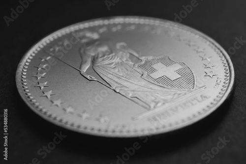 1 Swiss Franc coin closeup. Black and white background or wallpaper about economy, business or taxes. Money and Central Bank in Switzerland. Blurred figure of Helvetia, focus on the cross. Macro
