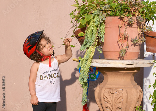 Little girl in a bike helpet is playing in the backyard with plants and watering them photo