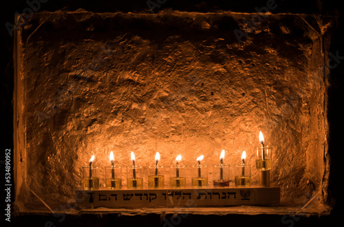 Glass vials hold oil and burning wicks that reflect a glowing light off a stone wall on the eighth night of the Jewish festival of Hanukkah in Jerusalem. photo