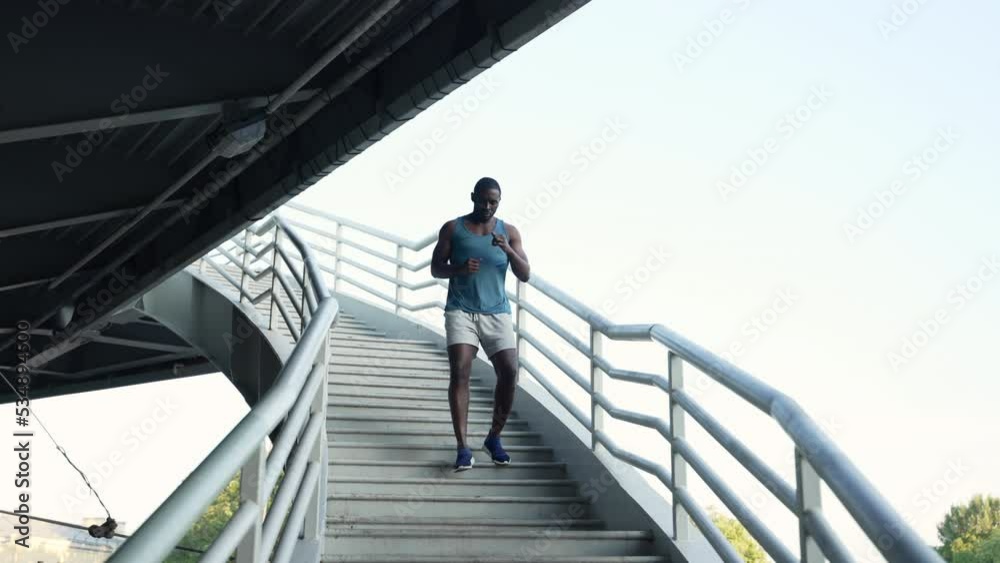 4k Male athlete is doing cardio activity and running on bridge in city spbas. Young african man goes down stairs and runs actively, does fitness and poses in modern town. One muscular guy is 4k Male athlete is doing cardio activity and running on bridge in city spbas. Young african man goes down stairs and runs actively, does fitness and poses in modern town. One muscular guy is