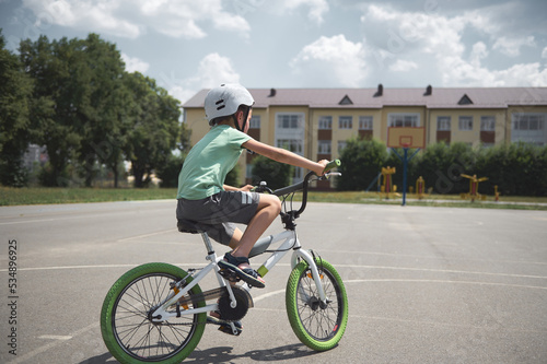 View from the back of an active sporty boy in sports helmet confidently riding bike. Caucasian school age child cycling on the city asphalt road. Healthy lifestyle. Physical exercises. Motion. Extreme