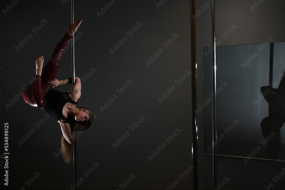 The dancer on the pylon in the studio. Girl doing exercises on a sports equipment. The dancer on the pylon in the studio. Girl doing exercises on a sports equipment.