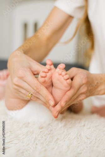 A loving mother holds in her caring hands the legs and fingers of a small newborn  a sleeping child on the bed in close-up. Selective focus. Women s happiness.