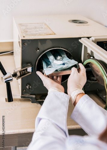 Close up of hands with dental autoclave sterilizer machine. Dentist hands sterilizing tools with autoclave, dentist with dental autoclave, close up of dentist with steam sterilizer photo