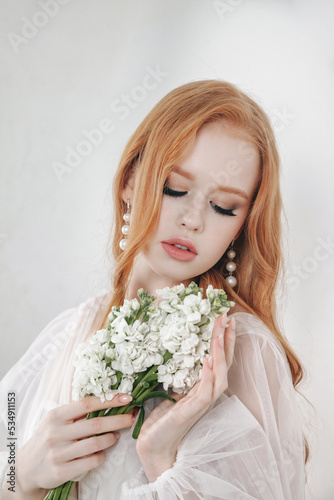 Portrait irish stylish bride young woman in white wedding dress with bouquet, closed eyes. Bride lady in vintage room on grey wall background in studio. Fashion style concept. Copy text space