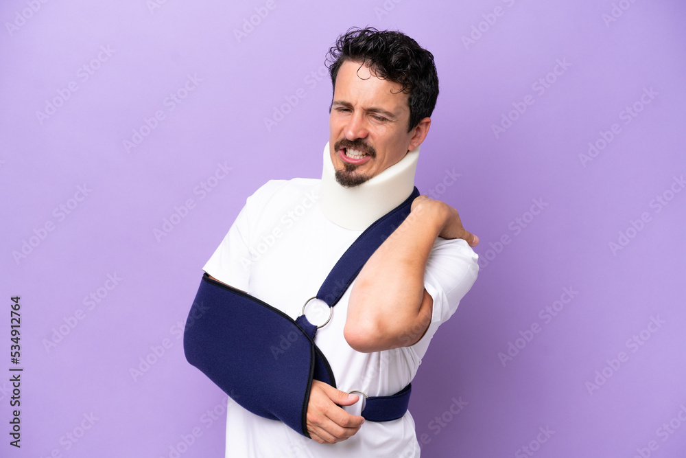 Young caucasian man wearing a sling and neck brace isolated on purple background suffering from pain in shoulder for having made an effort