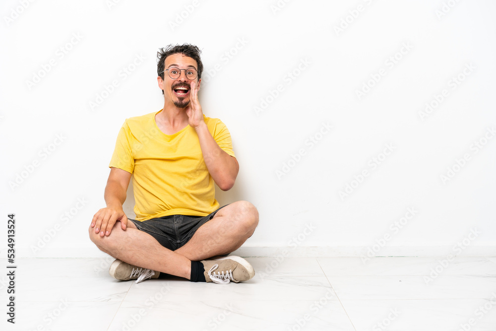 Fototapeta premium Young caucasian man sitting on the floor isolated on white background shouting with mouth wide open