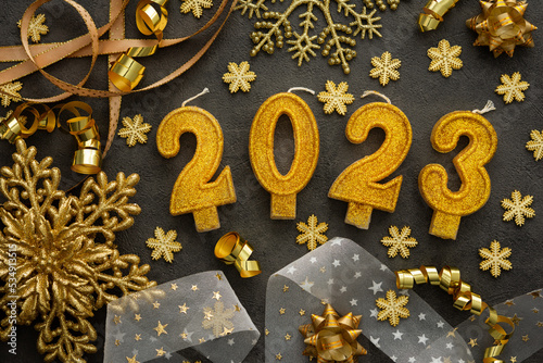 Merry Christmas and Happy New Year 2023, 2023 cake candles and various holiday decorations and ribbons in gold color on black background © pundapanda