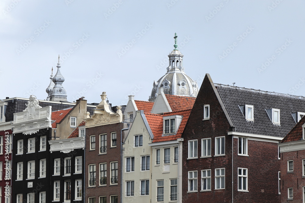 Amsterdam Damrak Canal Historic House Facades with Church Towers in the Background Close Up, Netherlands Amsterdam Damrak Canal Historic House Facades with Church Towers in the Background Close Up, Netherlands