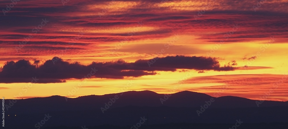 Atardecer en la Sierra de Guadarrama en Madrid, España. Cielo anaranjado con los últimos rayos de sol destacando la silueta de las montañas situadas al norte de Madrid.