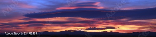 Atardecer en la Sierra de Guadarrama en Madrid, España. Cielo anaranjado y azul con una nube lenticular sobre la silueta de las montañas situadas al norte de Madrid.