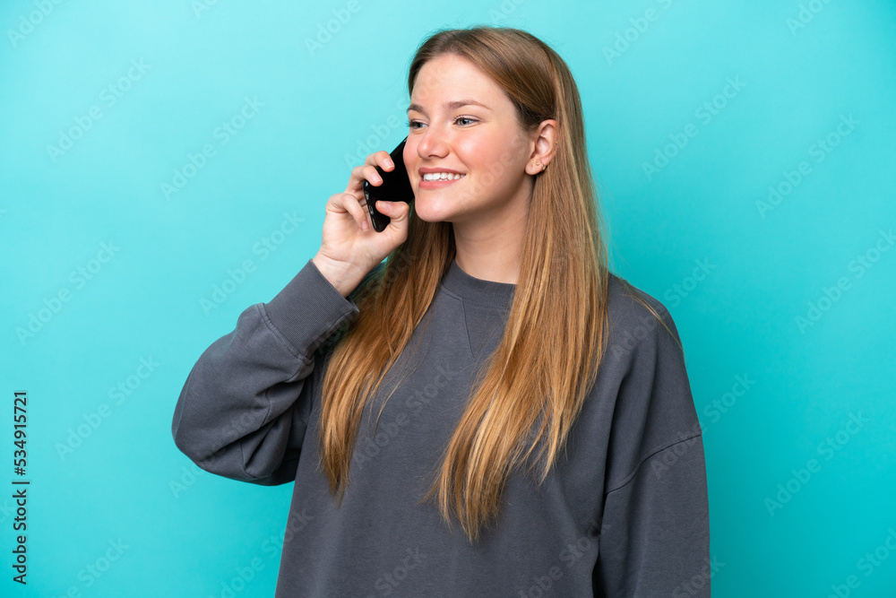 Fototapeta premium Young caucasian woman isolated on blue background keeping a conversation with the mobile phone
