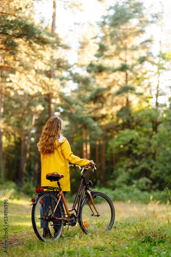 Beautiful happy woman in yellow coat riding bicycle in autumn park. Autumn fashion. Lifestyle. Relax  nature concept.