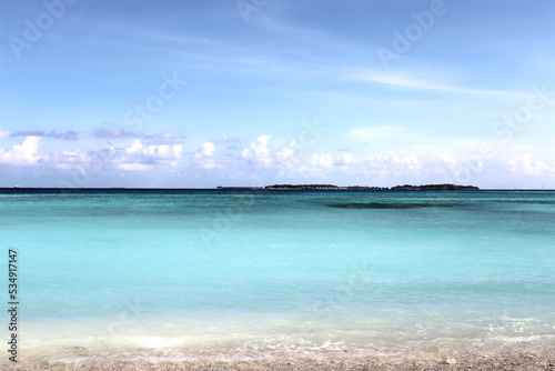 View from the beach to the Indian Ocean in the Maldives. On the horizon are houses on the water.