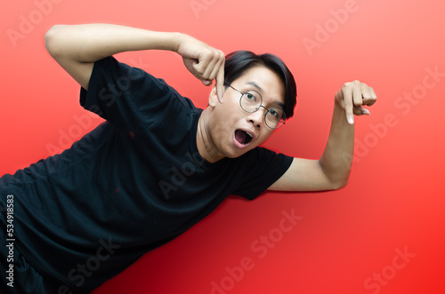 asian young man with glasses shocked happily pointing, and presenting something good isolated over red background. billboard advertisment model concept. © Teo