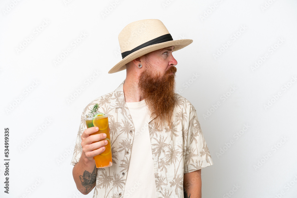Redhead man with long beard drinking a cocktail on a beach isolated on white background looking to the side Redhead man with long beard drinking a cocktail on a beach isolated on white background looking to the side