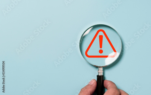 Hand holding magnifier glass with red triangle caution warning sign for focus notification error and maintenance concept. photo