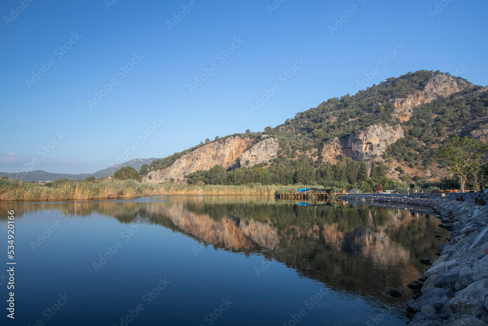 The rock-cut temple tombs of the ancient city of Kaunos in Dalyan, Muğla, Turkey. Beautiful view of Dalyan river with reed beds, excursion boats and carved tombs in the background.