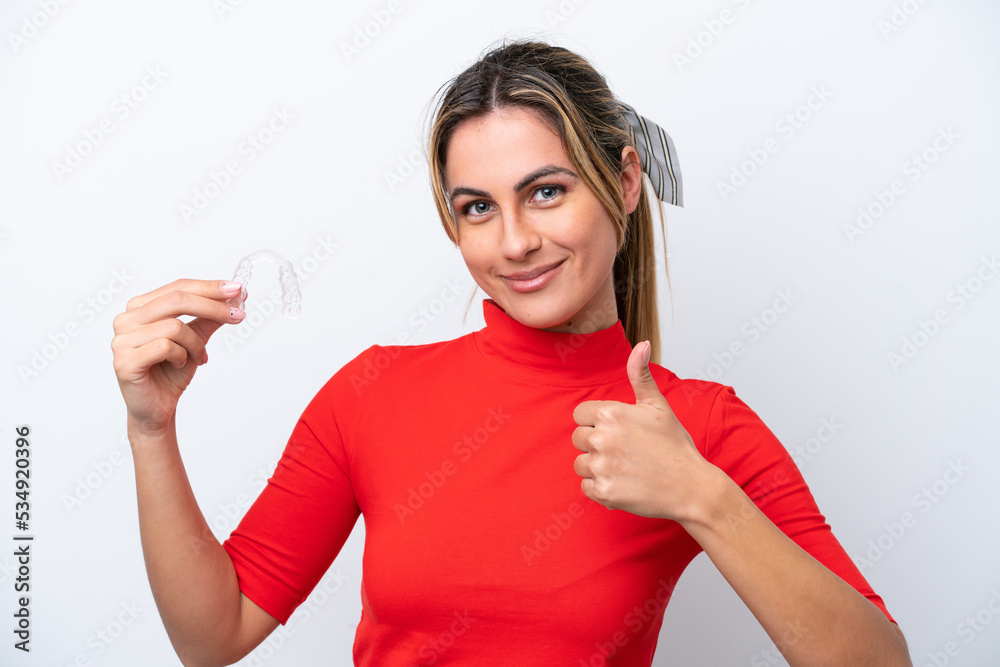 Young caucasian woman holding invisible braces on white background with thumbs up because something good has happened Young caucasian woman holding invisible braces on white background with thumbs up because something good has happened