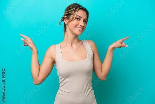 Young caucasian woman isolated on blue background pointing finger to the laterals and happy