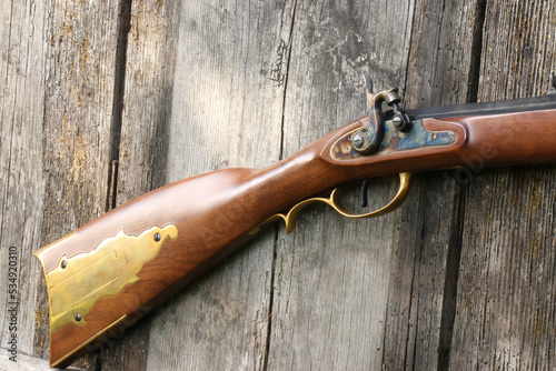 A close-up of the percussion lock and the stock of a Kentucky rifle on an old plank background photo